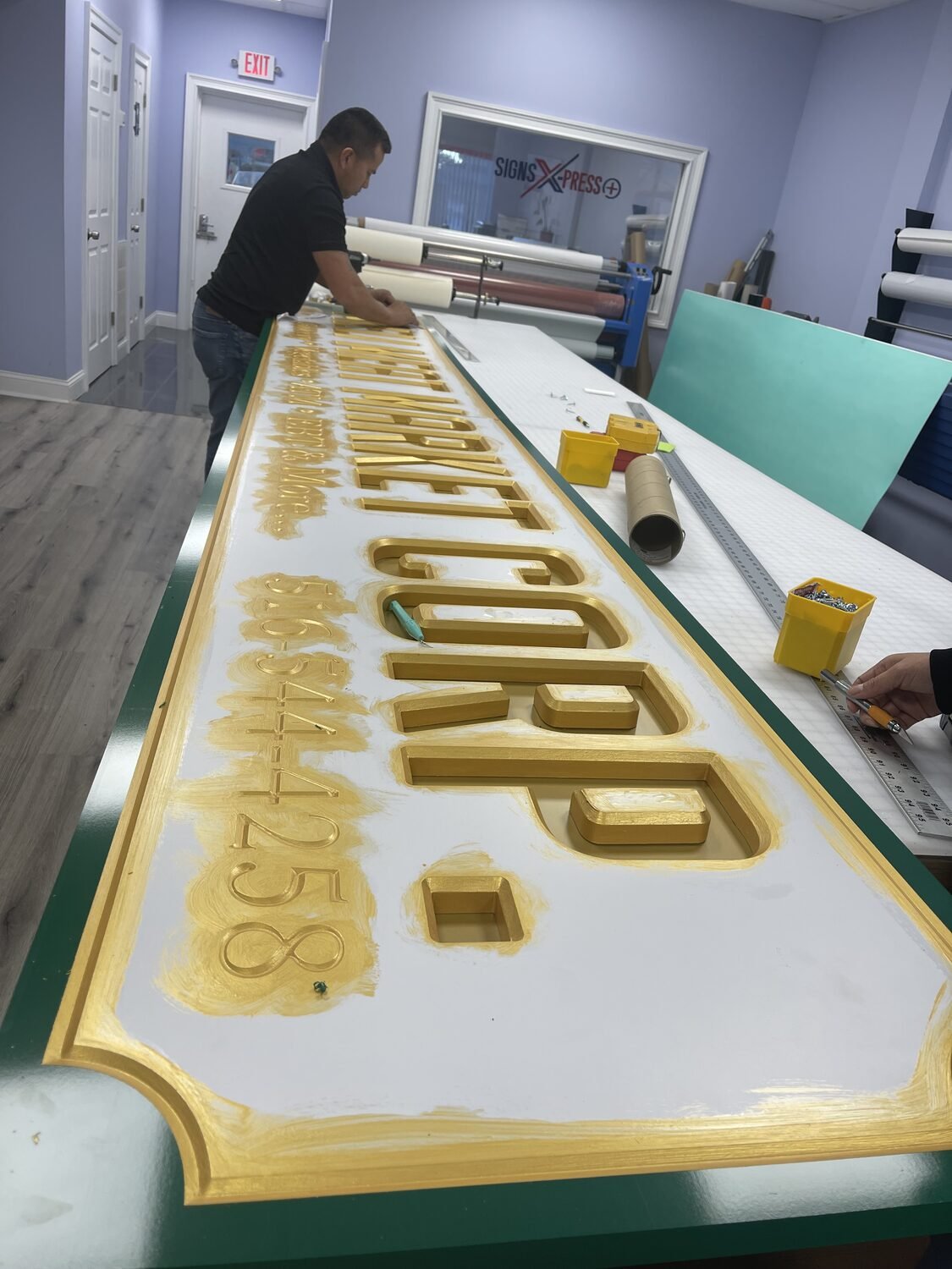 Gold leaf being laid on a carved sign in the shop